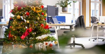 Árbol de Navidad decorado con bolas rojas y doradas junto a un escritorio de oficina, ejemplo de decoración navideña corporativa