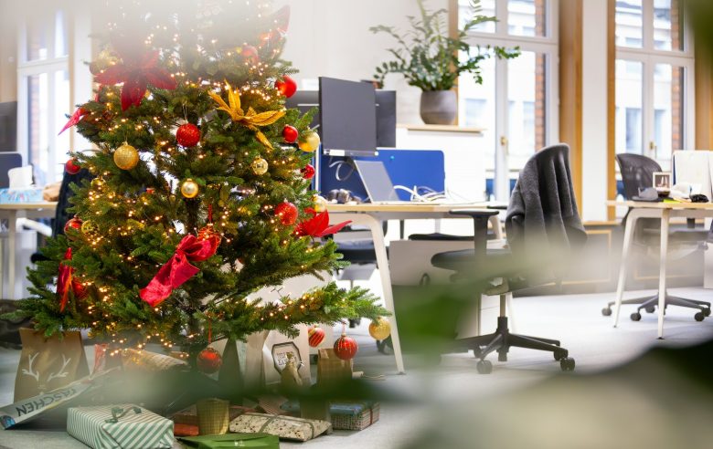 Árbol de Navidad decorado con bolas rojas y doradas junto a un escritorio de oficina, ejemplo de decoración navideña corporativa