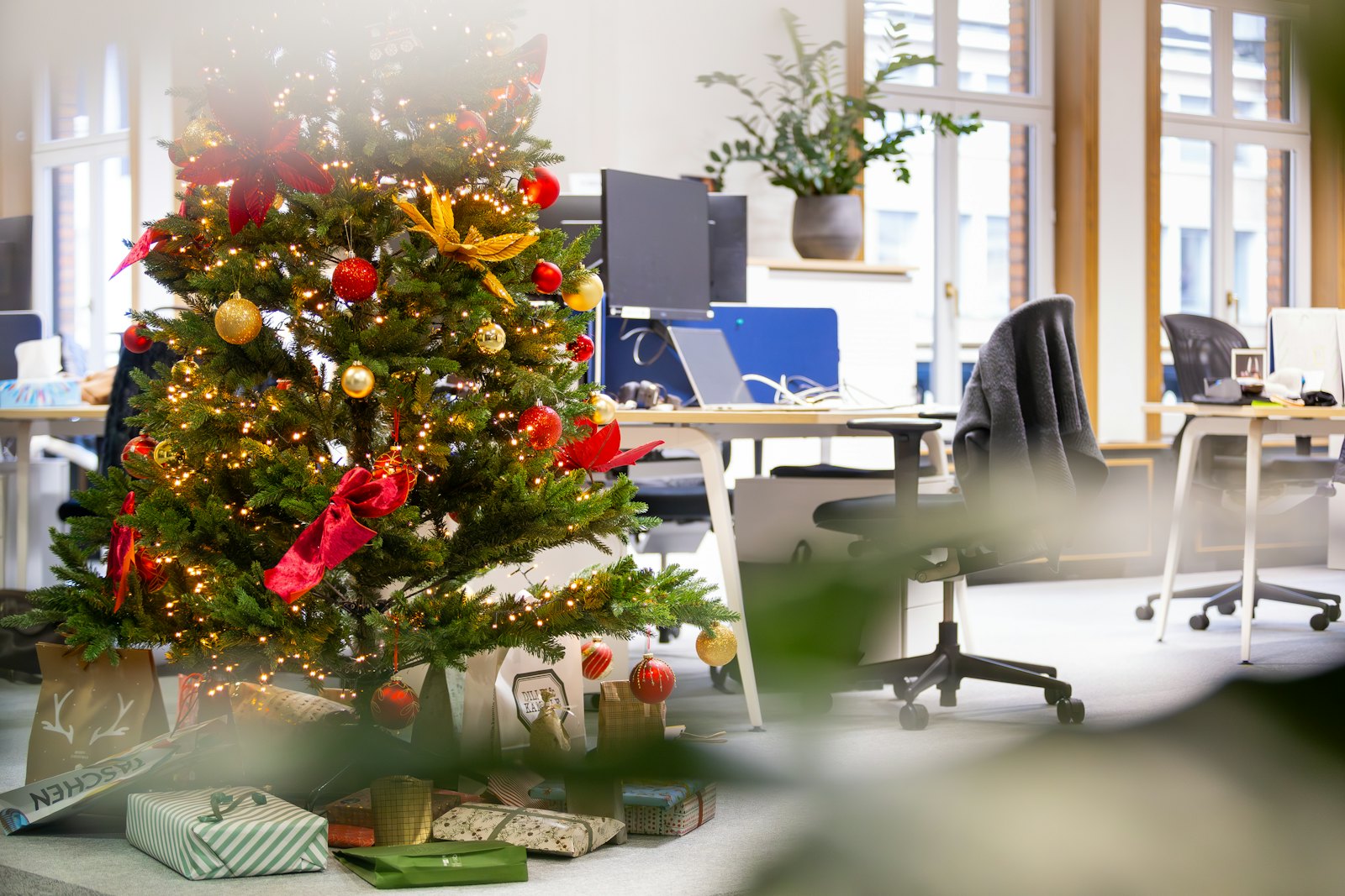Árbol de Navidad decorado con bolas rojas y doradas junto a un escritorio de oficina, ejemplo de decoración navideña corporativa